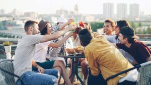 Diverse group of friends toasting with drinks on a sunny rooftop gathering.